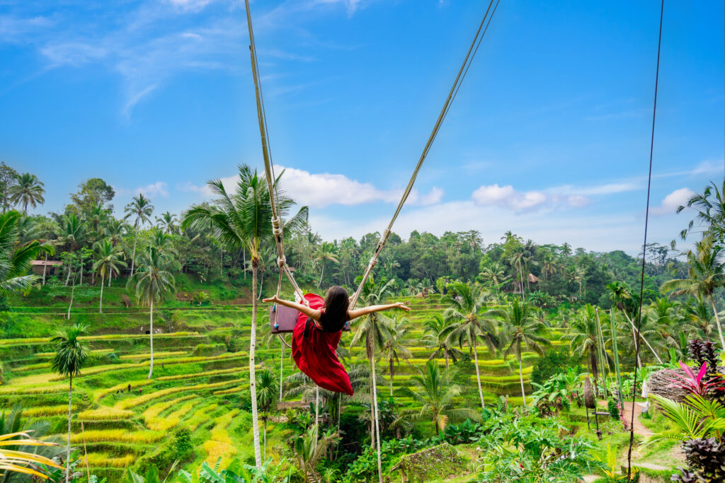 Young female tourist in red dress enjoying the Bali swing at tegalalang rice terrace in Bali, Indonesia